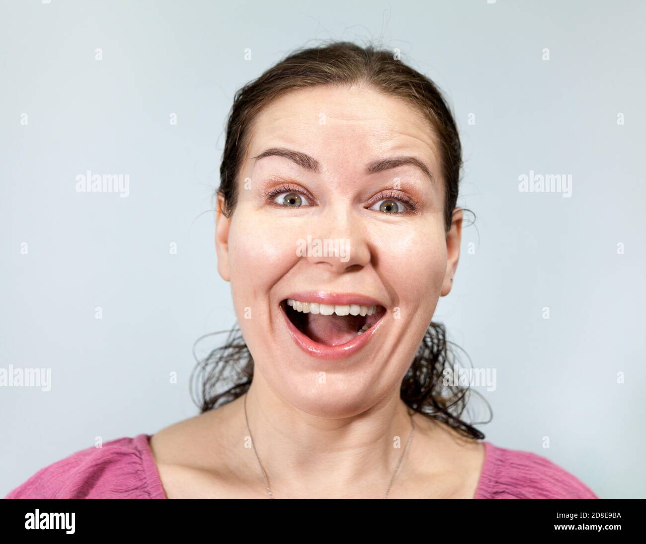 Ein breites, dummes Lächeln auf dem Gesicht der kaukasischen Frau, die sich in ein Lachen verwandelt, Porträt auf grauem Hintergrund, Emotionsreihe. Stockfoto