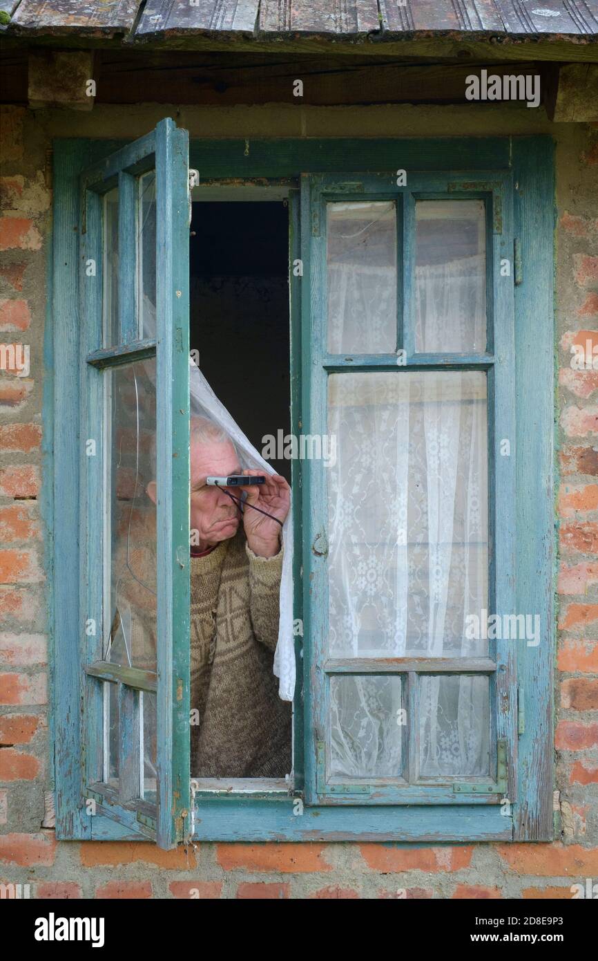 Miserable suchen älter männlich Vorhang twitcher Spionage auf Nachbarn aus Fenster, um jemanden zu finden, der die Regeln für die Sperrung einer Coronavirus-Pandemie bricht Stockfoto