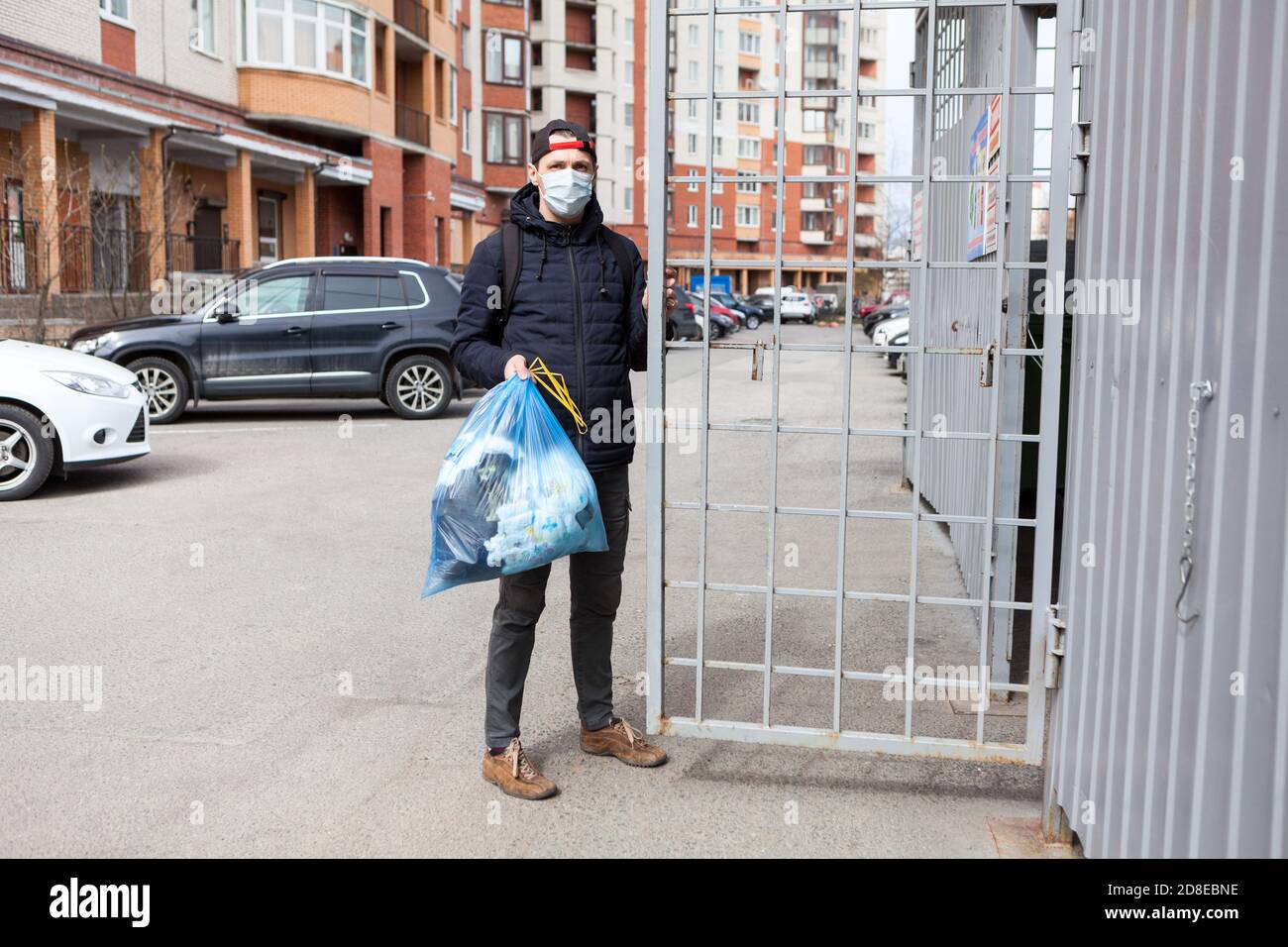 Erwachsene kaukasischen Mann trägt medizinische Maske aus dem Müll Um die Einschließung eines Wohnhauses zu entsorgen Stockfoto