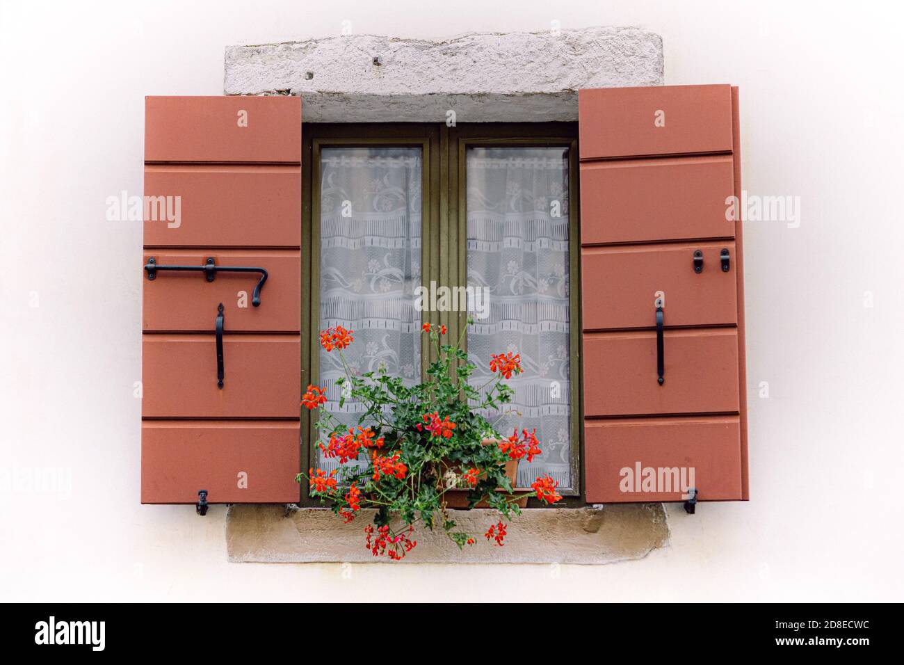 Italienisches Hausfenster mit offenen roten Schließungen und roten Geranien Stockfoto