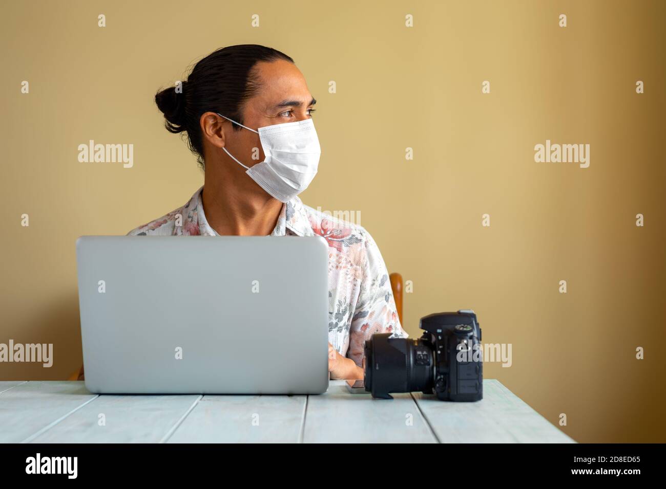 Latino Fotograf mit medizinischer Maske arbeitet zu Hause. Speicherplatz kopieren. Coronavirus-Konzept. Stockfoto