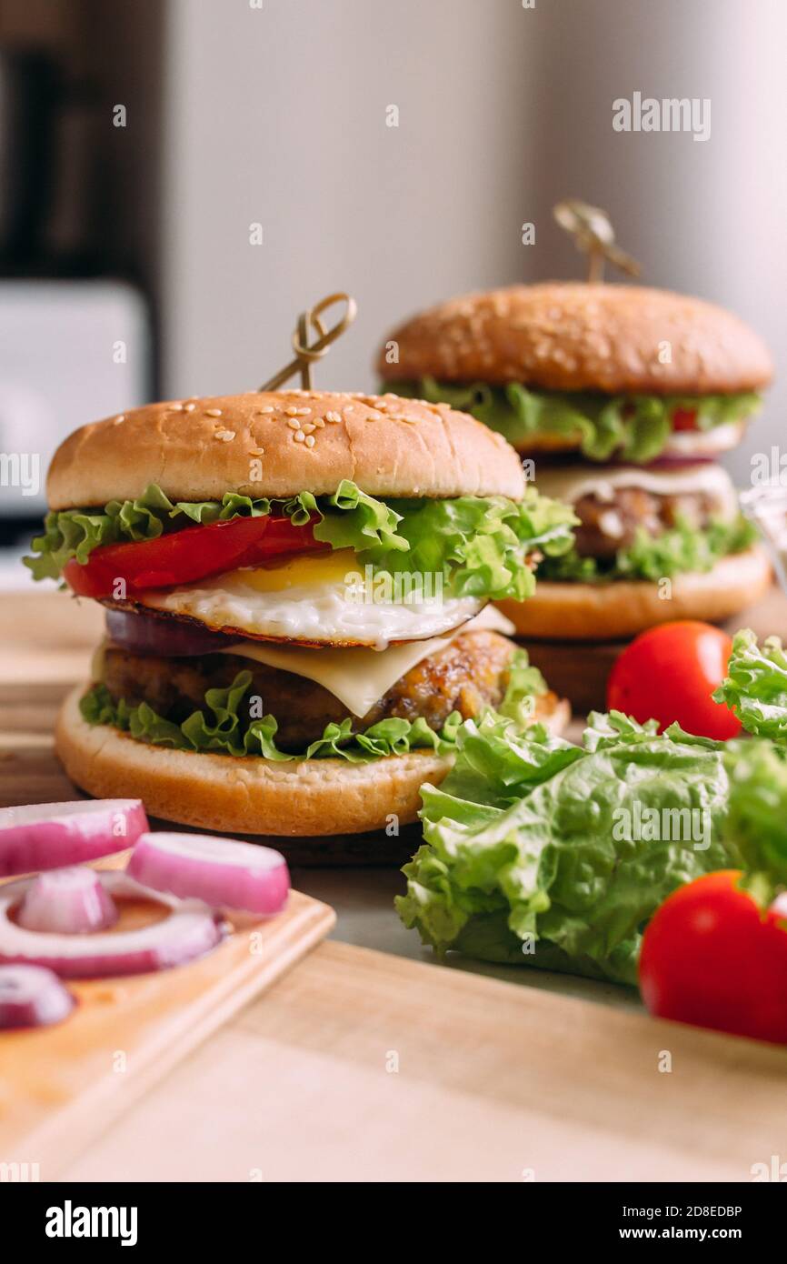 Zwei hausgemachte frische, leckere Burger mit Salat und Käse. Zutaten auf dem Tisch. Heller Hintergrund für Speisen. Stockfoto