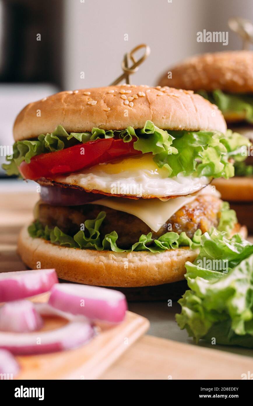 Zwei hausgemachte frische, leckere Burger mit Salat und Käse. Zutaten auf dem Tisch. Heller Hintergrund für Speisen. Stockfoto