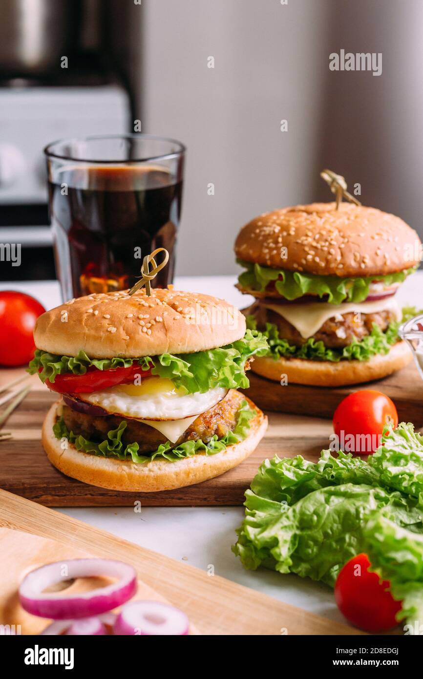 Zwei hausgemachte frische, leckere Burger mit Salat und Käse. Zutaten auf dem Tisch. Heller Hintergrund für Speisen. Stockfoto