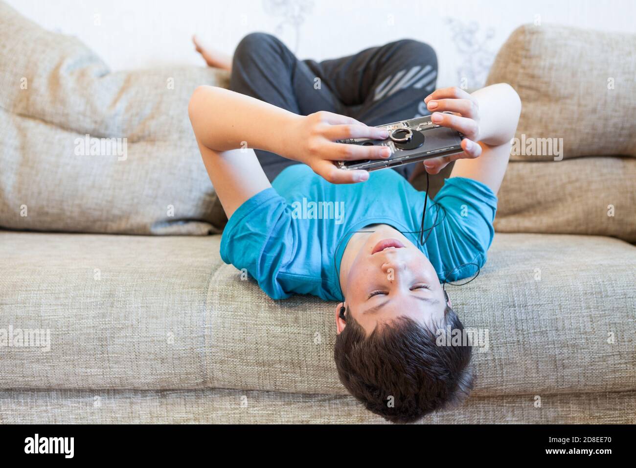 Porträt eines kaukasischen Teenagers mit großem Smartphone oder Spielkonsole in den Händen, der über soziale Medien spielt oder sich einlässt, während er auf dem Sofa liegt Stockfoto