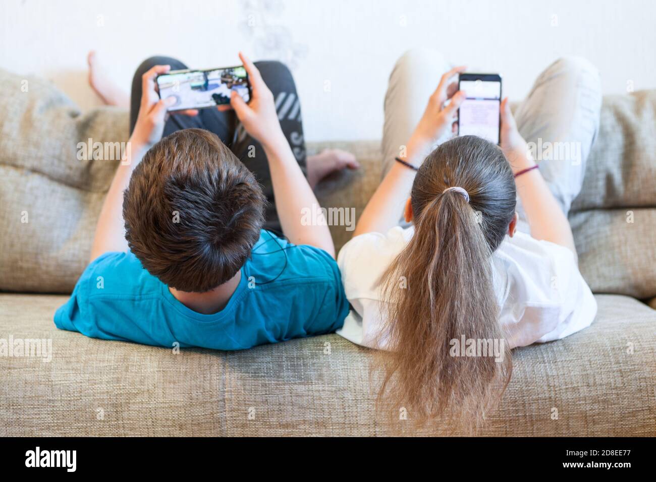 Schwester und Bruder benutzen ihre Smartphones, während sie sich zurücklehnen Eine Couch zu Hause Stockfoto