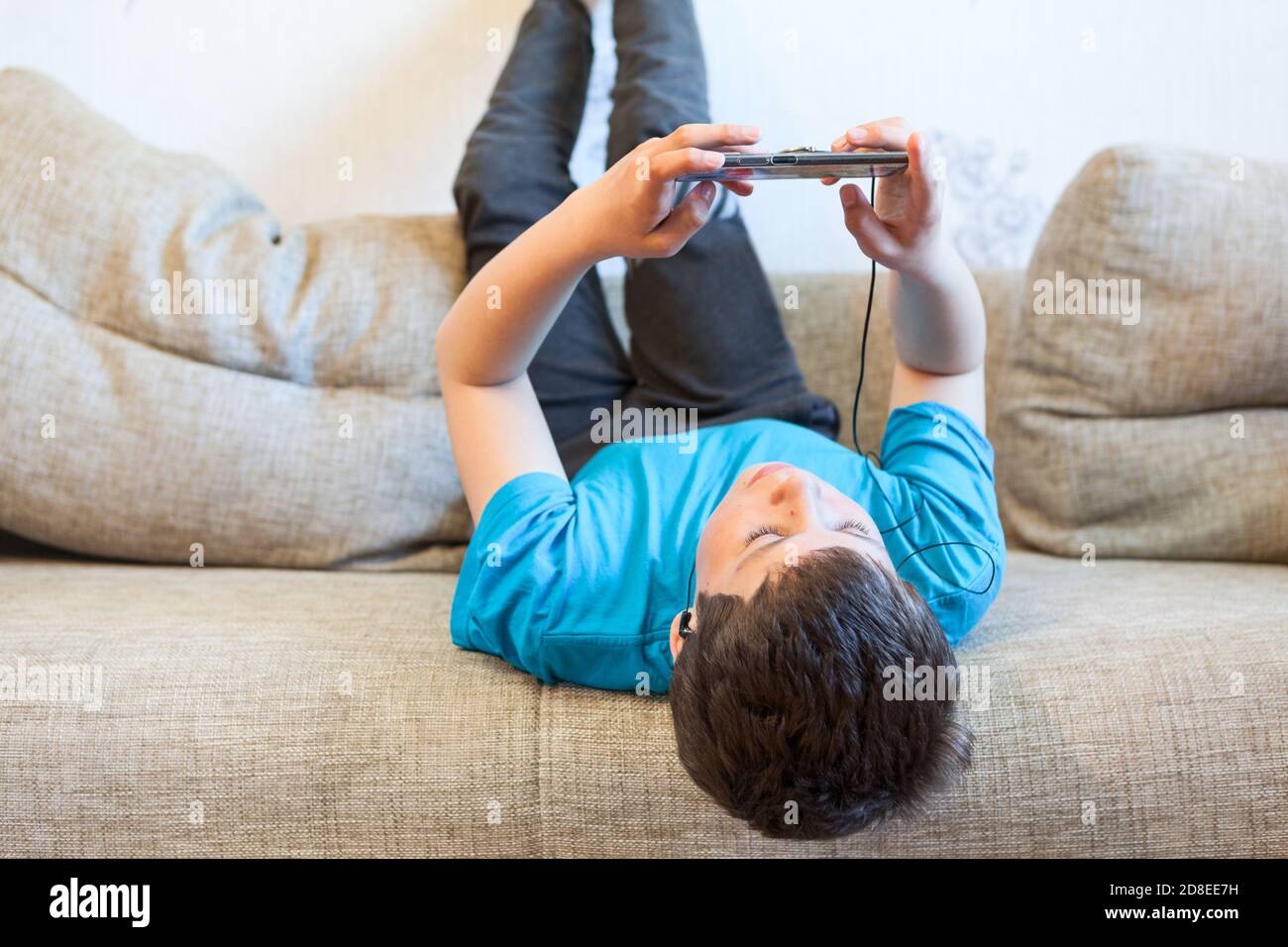 Faul preteen Junge Spiel mit seinem Handy, Kind liegt zurück auf der Couch in einem heimischen Zimmer Stockfoto