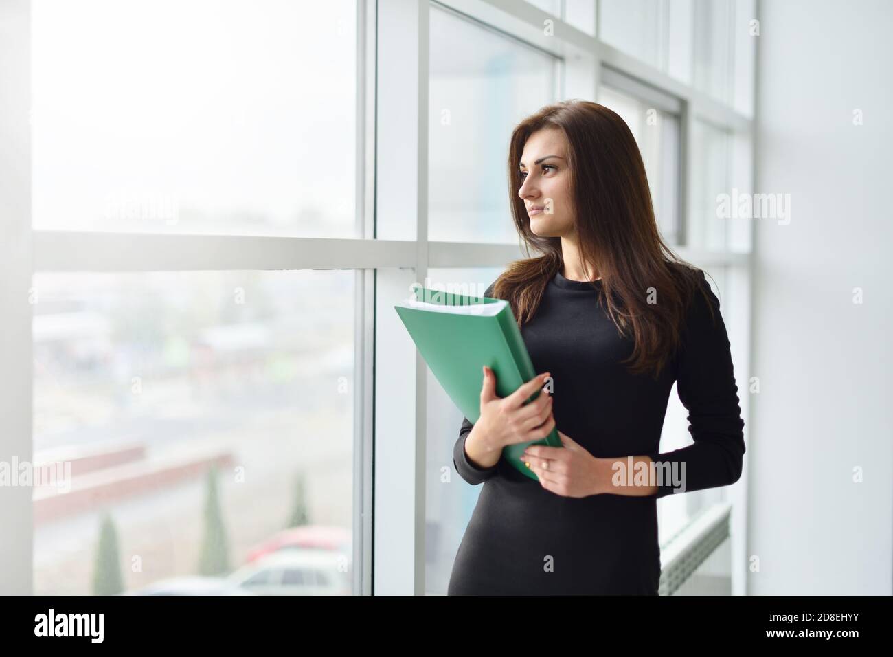 Eine junge zielgerichtete Geschäftsfrau mit einem Paket von Dokumenten Blick aus einem Fenster im Büro Stockfoto