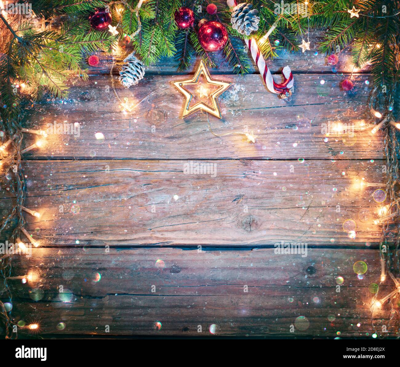 Rustikales Weihnachtsbrett - Fir Zweige Und String Licht An Holzplanke Mit Defokussierten Abstrakten Schneefall Stockfoto