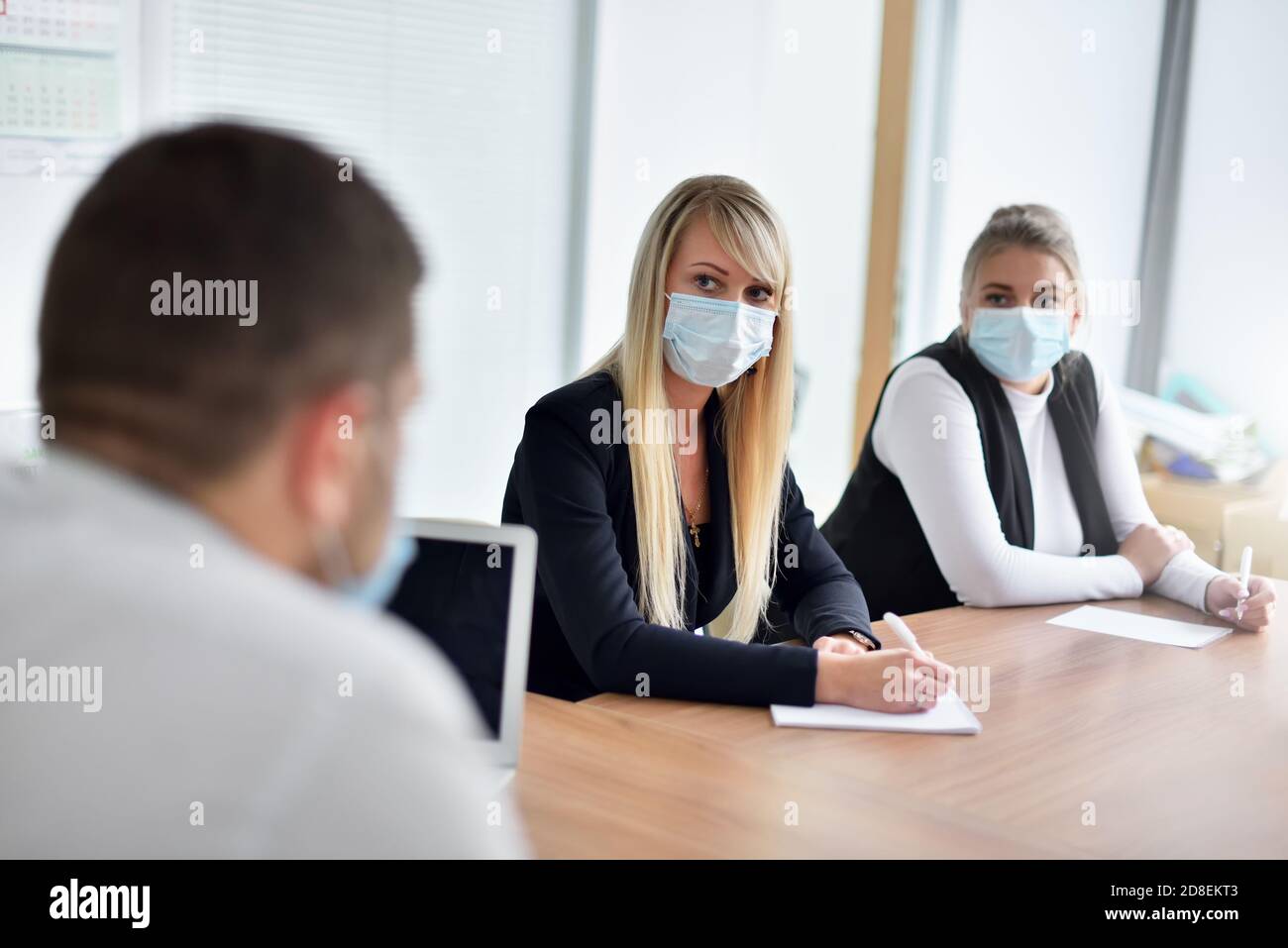 Junge Mitarbeiterin in Gesichtsmaske Blick auf CEO an Meeting im Büro Stockfoto