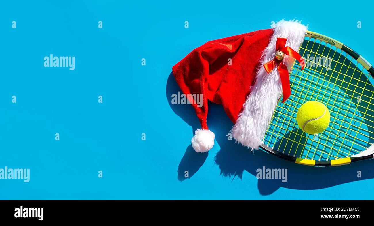 Weihnachtsmann Hut auf Tennisschläger und Ball auf blauem Hintergrund. Frohe Weihnachten und Happy New Year Tennis Konzept. Nahaufnahme, Sport-Lifestyle, lustig. Stockfoto