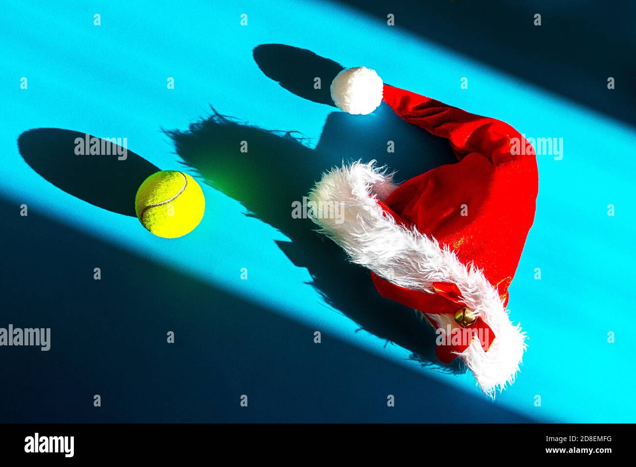 Weihnachtsmann Hut auf Tennisschläger und Ball auf blauem Hintergrund. Frohe Weihnachten und Happy New Year Tennis Konzept. Nahaufnahme, Sport-Lifestyle, lustig. Stockfoto