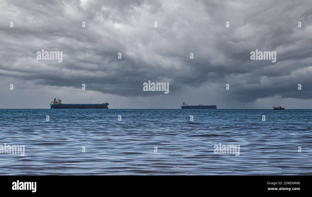 Nahaufnahme einer bewölkten Meereslandschaft an einem regnerischen Sommertag. Blaues Meer, Sturmwolken über dem Horizont und mehrere Frachtschiffe Stockfoto