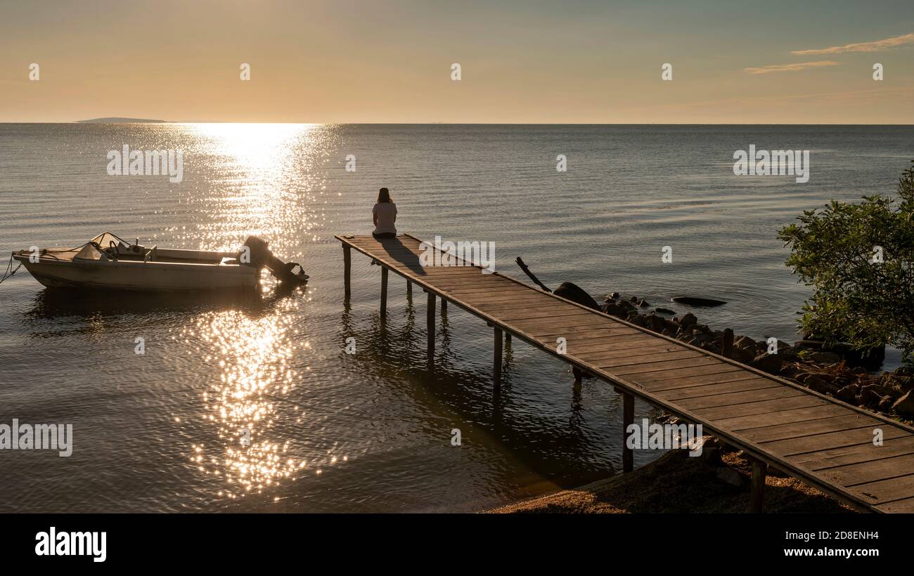 Einsame junge Frau sitzt auf einem Pier, entspannen und genießen den Sonnenuntergang am Razim See, Rumänien Stockfoto