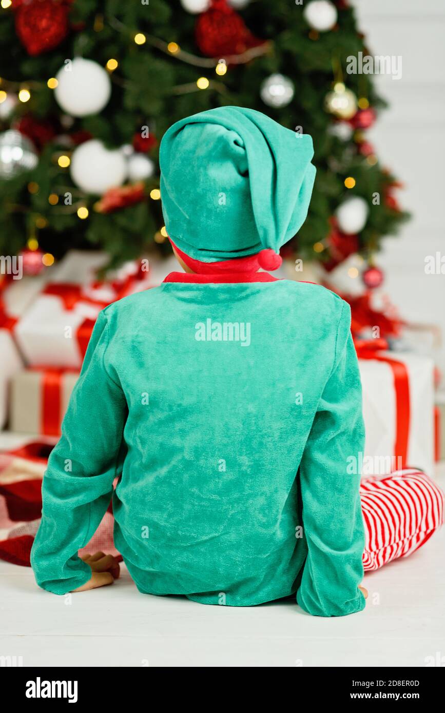 Junge öffnen Geschenke unter Weihnachten Baum auf Morgen. Kleinkind Junge sitzt auf dem Boden öffnen Geschenke. Kind unter dem Weihnachtsbaum mit Geschenkboxen. Deco Stockfoto
