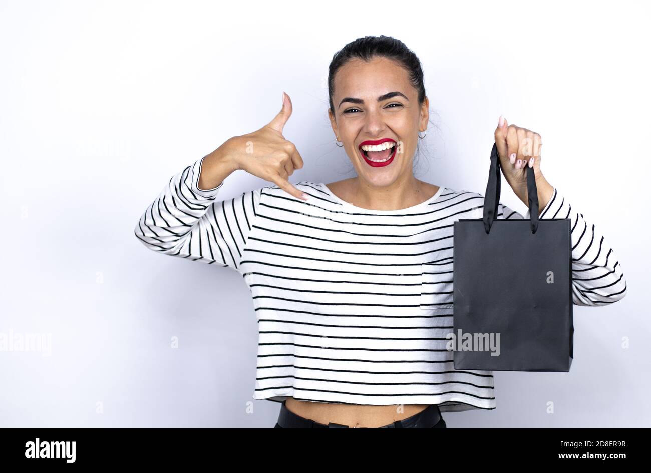 Junge schöne Frau hält eine schwarze Einkaufstasche schreien mit verrückten Ausdruck Rock-Symbol mit Händen oben tun. Schwarzer Freitag Stockfoto