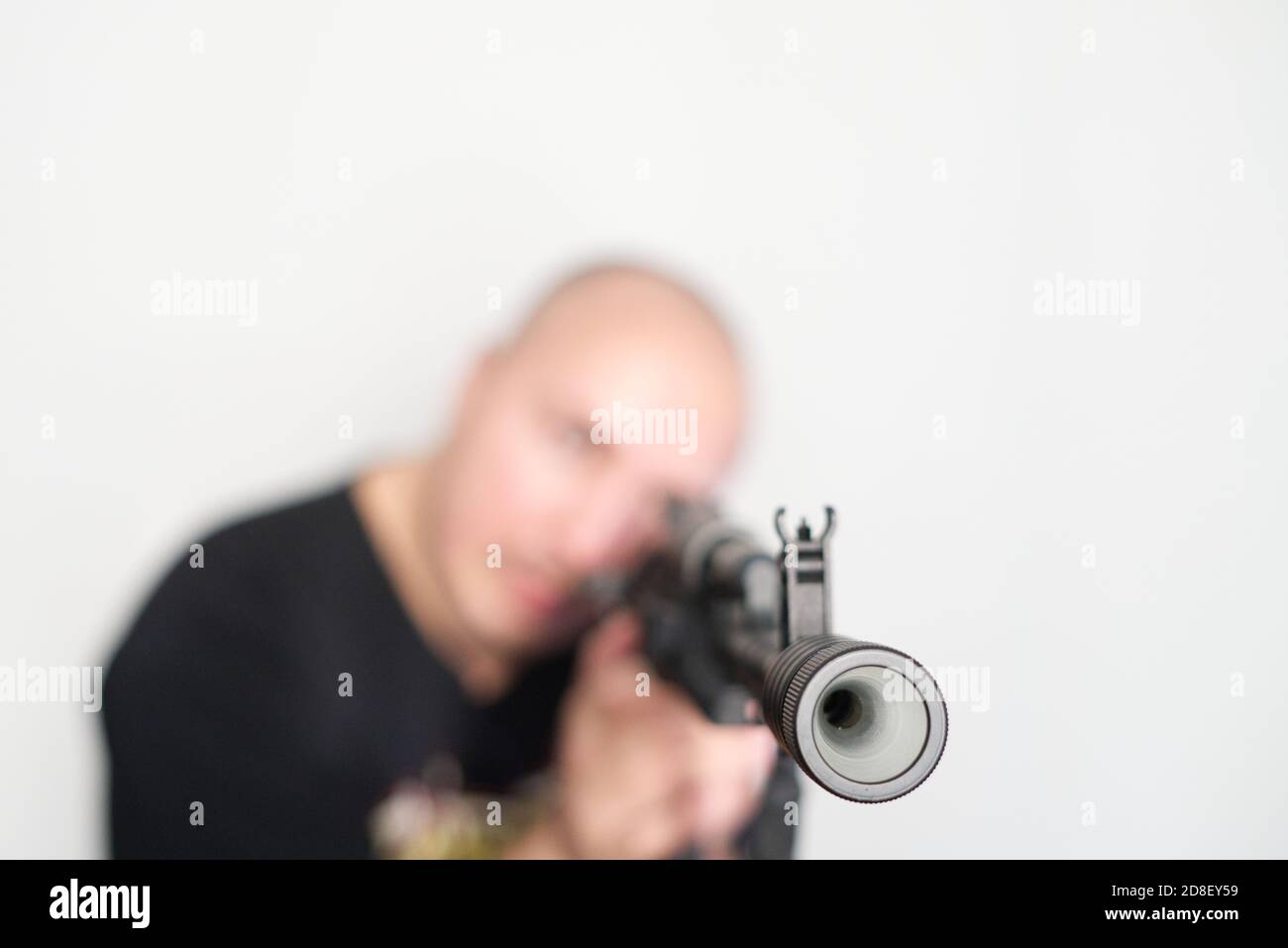 Schwerer verschwommener Mann auf hellem Hintergrund mit Gewehr in den Händen Stockfoto