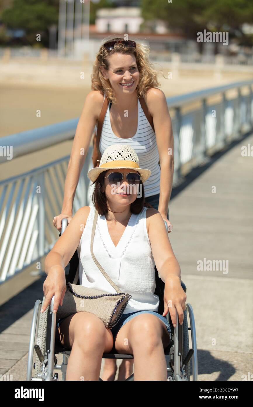 lady schiebt weibliche Freundin im Rollstuhl während im Sommerurlaub Stockfoto
