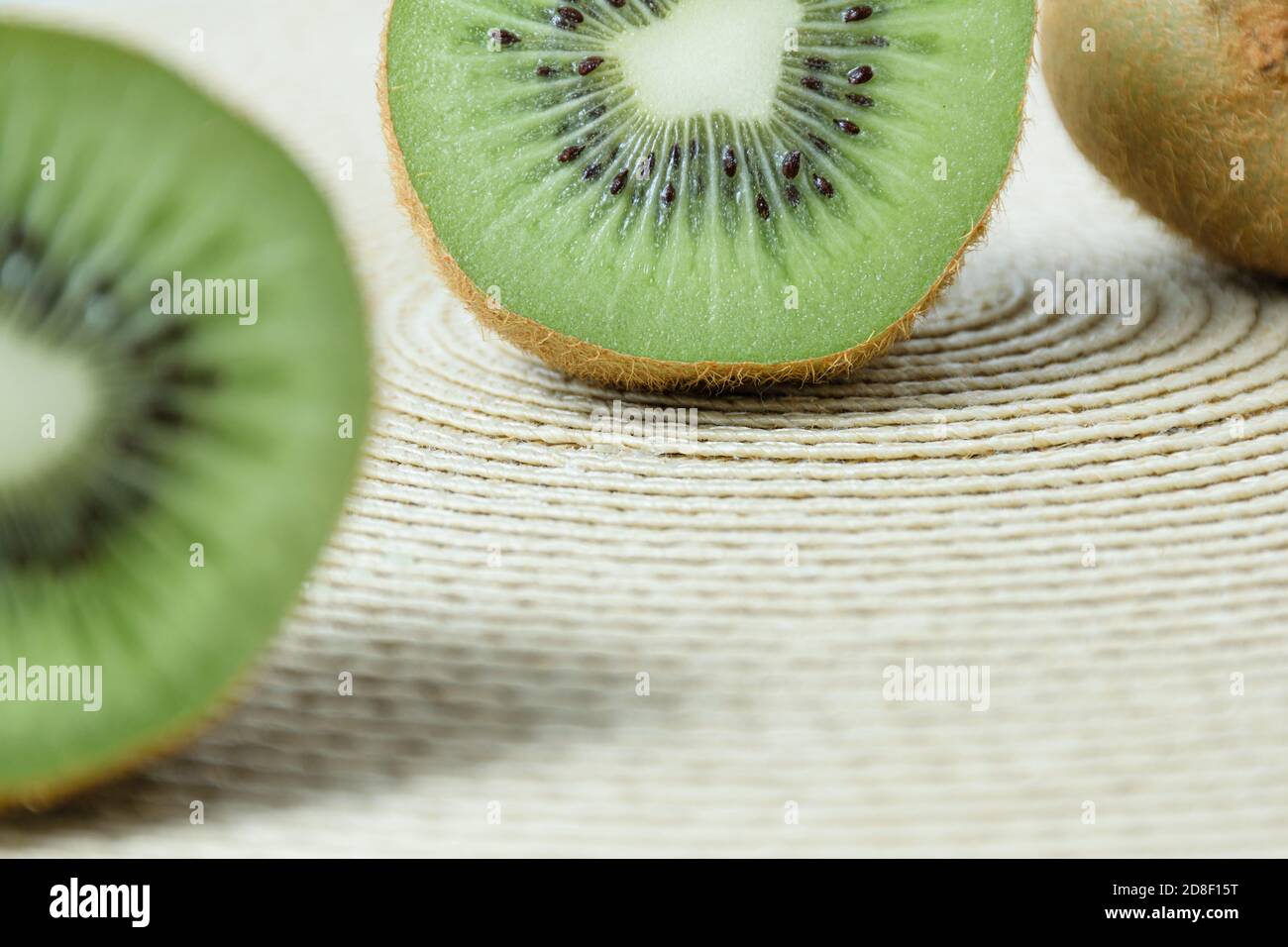 Eine halbe Kiwi entkochte im Vordergrund, im Hintergrund die andere Hälfte der Frucht auf einem Strohplacemat. Stockfoto