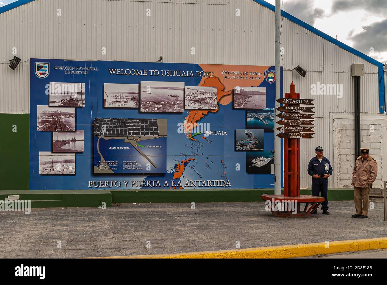 Ushuaia, Feuerland, Argentinien - 13. Dezember 2008: 1 Beamte am Eingang zum Hafen in der Nähe von großen blauen Begrüßungsplakat mit historischen Bildern von har Stockfoto