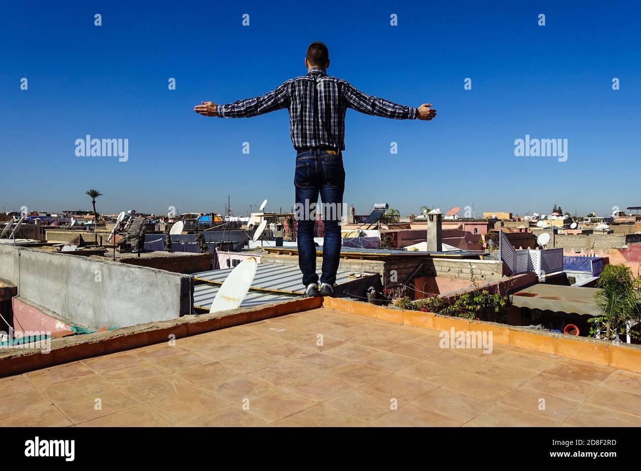 Junger weißer Mann in blauem karierten Hemd, der in Marrakesch, Marokko, am Rand eines Dachs mit quer verspreizenden Armen steht Stockfoto
