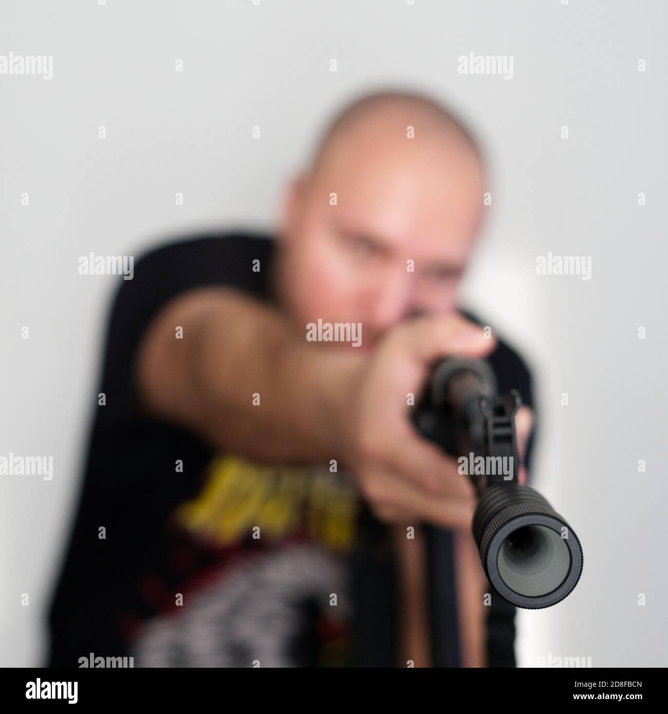Schwerer verschwommener Mann auf hellem Hintergrund mit Gewehr in den Händen Stockfoto