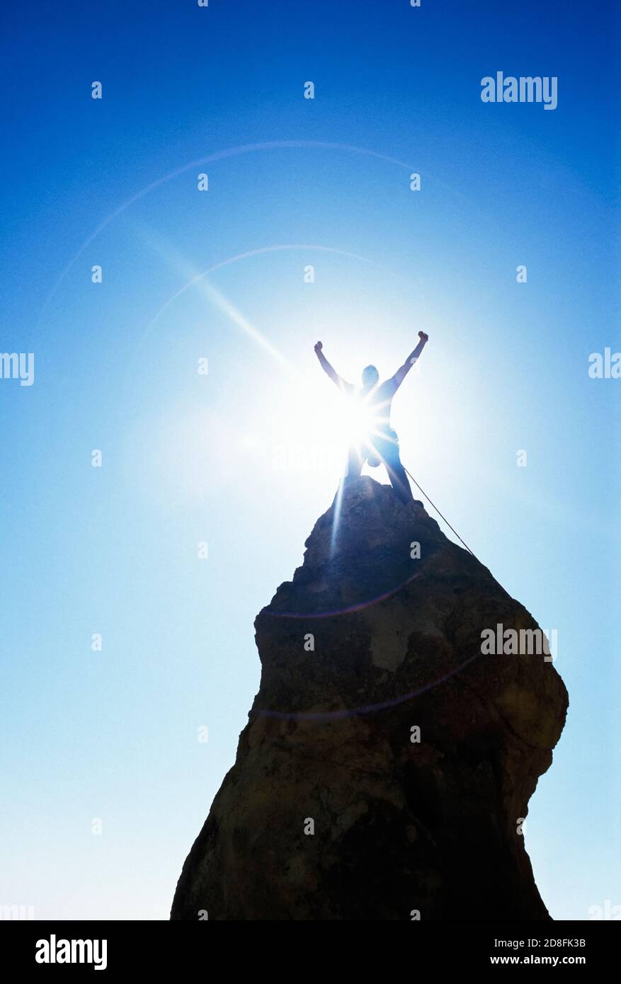 Ein Mann feiert mit den Händen über Kopf auf einem steilen Felsen Pinnacle mit der Sonne aufflammen von hinten. Stockfoto