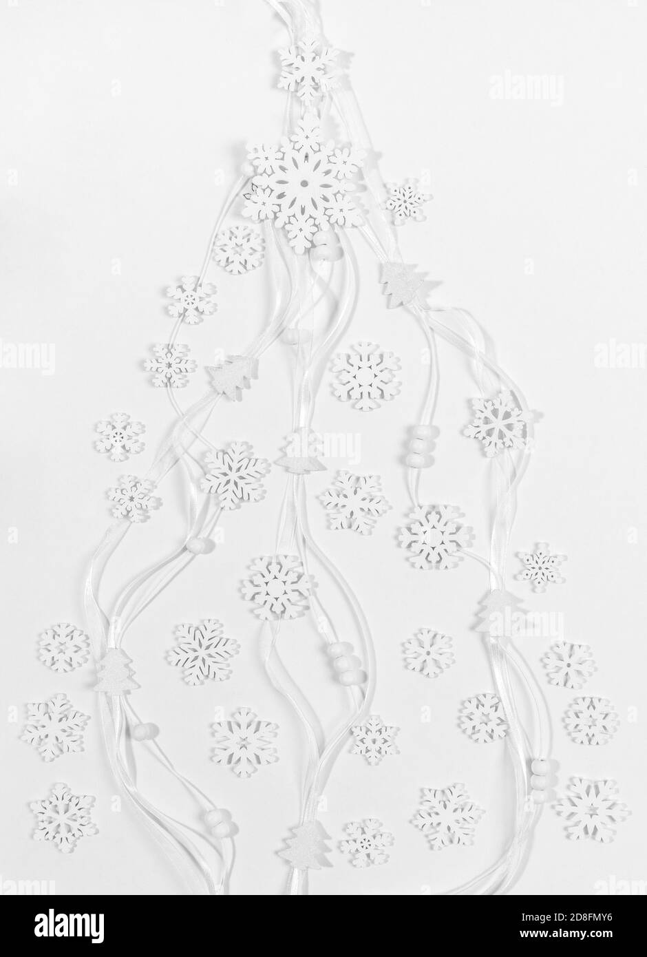 Weiße hölzerne Schneeflocken, kleine Weihnachtsbäume, runde Perlen auf schmalen Bändern liegen flach als kreativer Weihnachtsbaum. Stockfoto