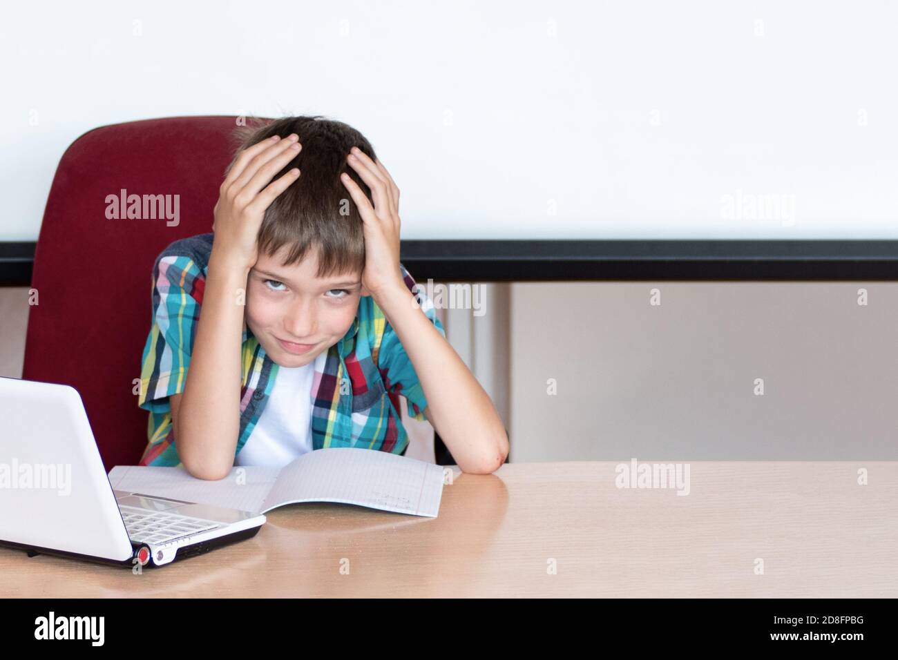 Müder Junge, der seinen Kopf hält, um Hausaufgaben zu machen. Kind mit Lernschwierigkeiten. Ein Junge, der Probleme mit seinen Hausaufgaben hat Stockfoto