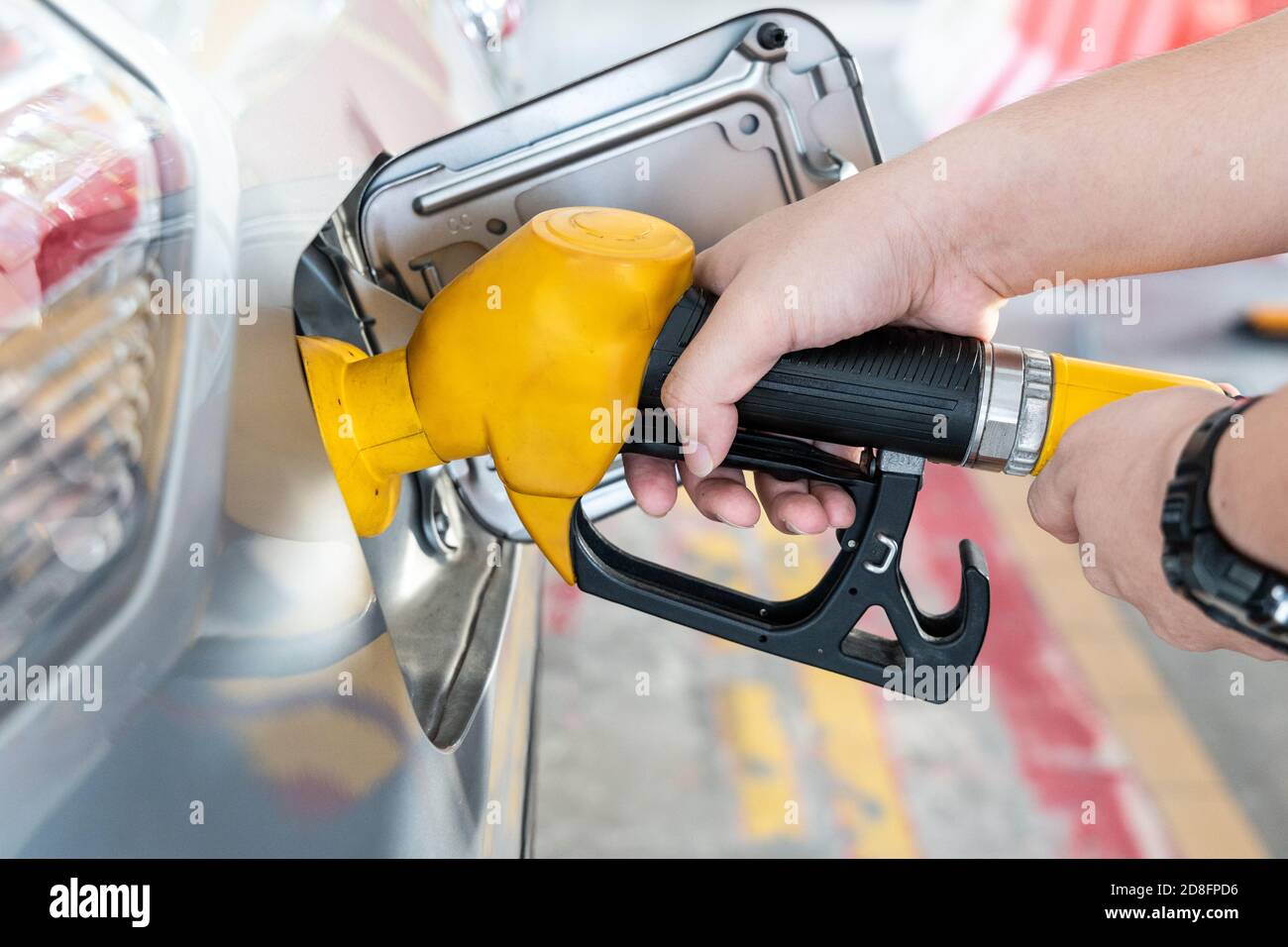 Gelbe Düse mit Handhaltung zum Tanken des Fahrzeugs bei Gas Station Stockfoto