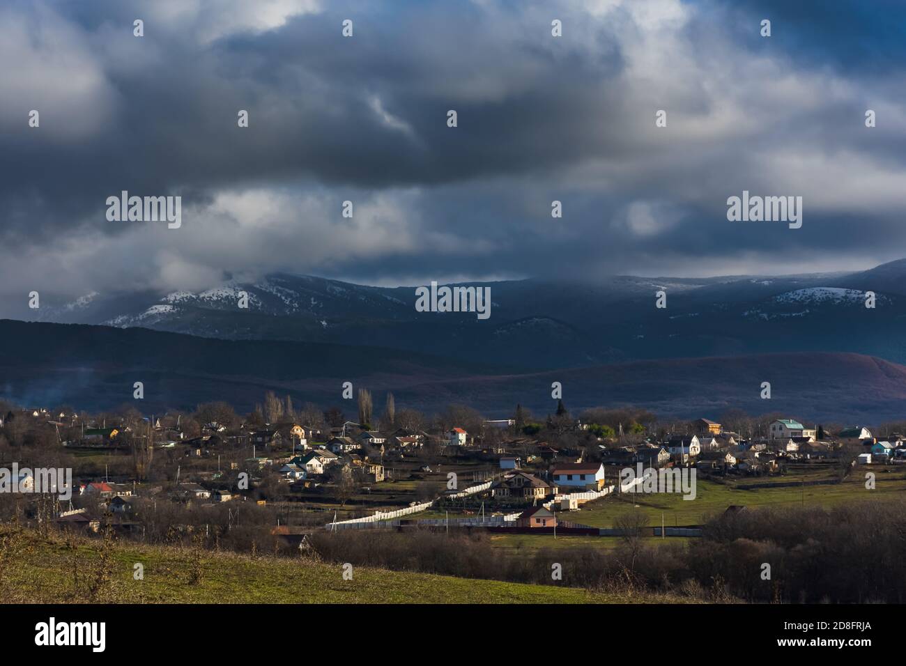 Winter ländliche Landschaft mit riesigen dunklen Wolken und schneebedeckten Bergen. Reise nach Russland. Winter ohne Schnee. Panoramablick auf das Dorf Peredo Stockfoto