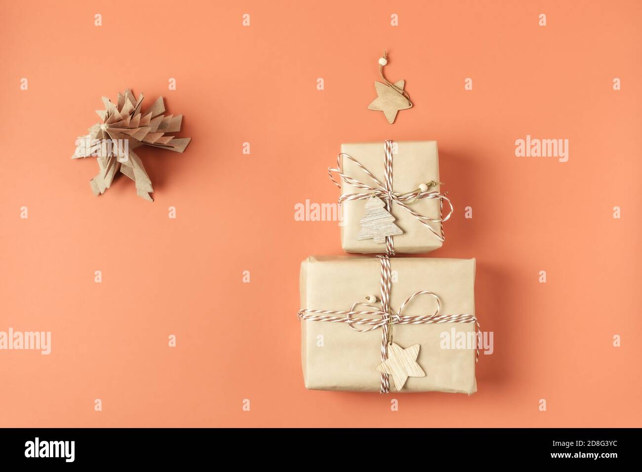 Zwei Weihnachtsgeschenke in Bastelpapier gehüllt liegen in Form von Weihnachtsbaum mit Holzstern auf Terrakotta-Hintergrund. Speicherplatz kopieren. Draufsicht. Stockfoto