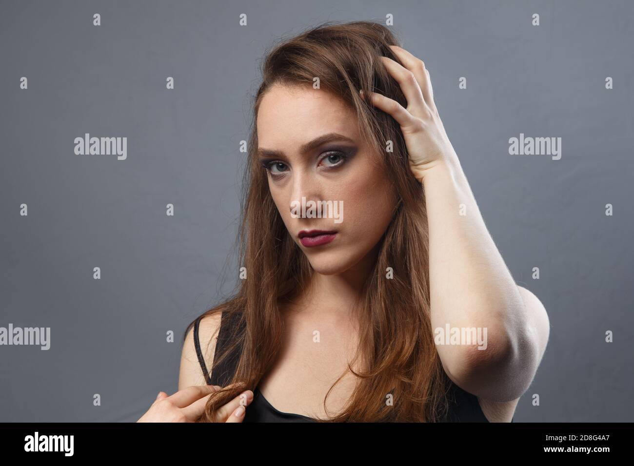 Foto von Mädchen berühren ihre Haare mit lila Lippen auf Grauer Hintergrund Stockfoto