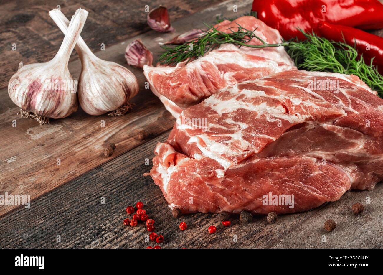 Rohes Schweinekotelett Steak und Knoblauch, Pfeffer auf Holzhintergrund. Hintergrund für das Essen. Rohes Fleisch auf einem Holzbrett Stockfoto