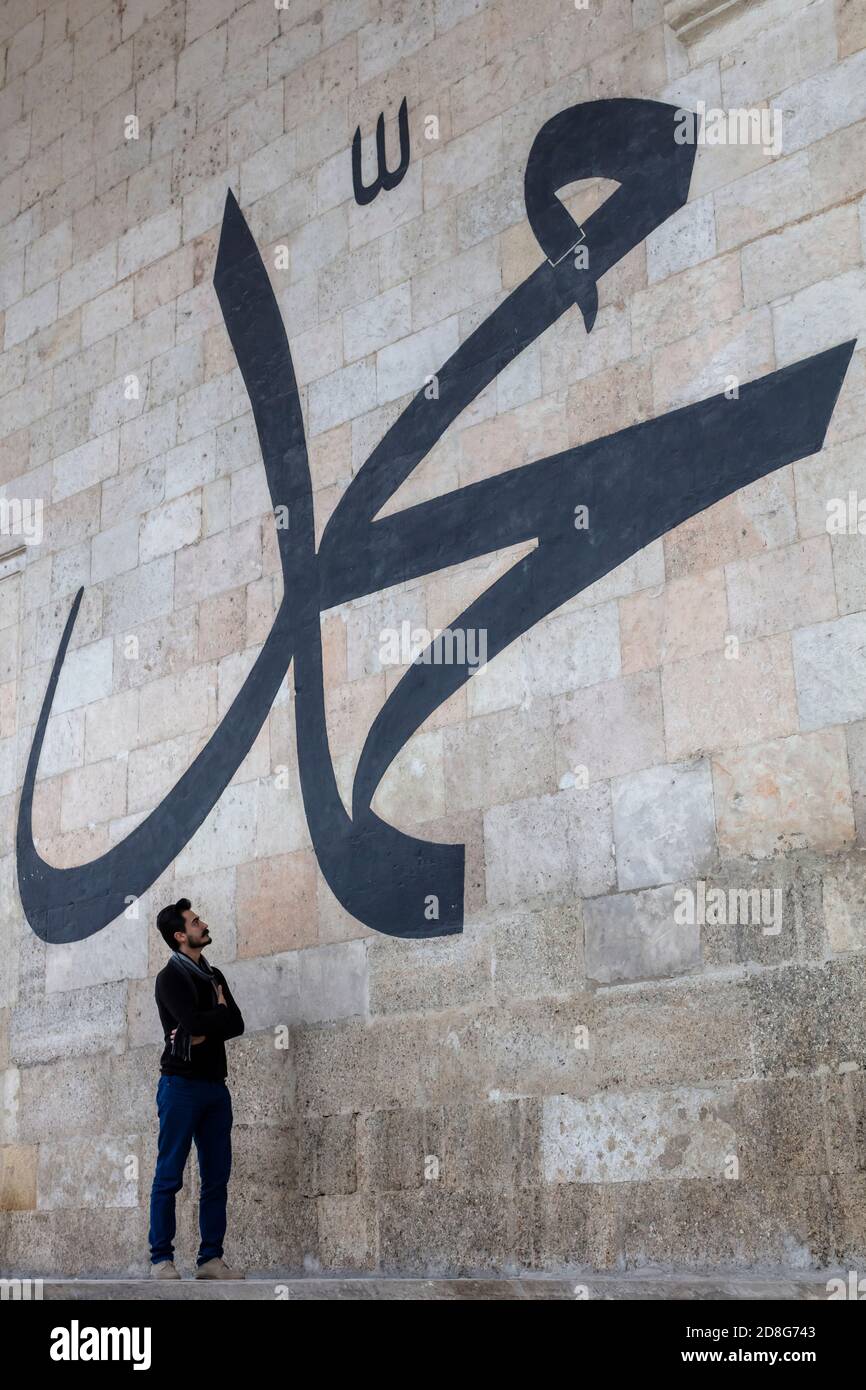 Junger Mann starrt auf die arabische Kalligraphie und bedeutet 'Prophet Muhammad' An der Mauer der alten Edirne Moschee Stockfoto