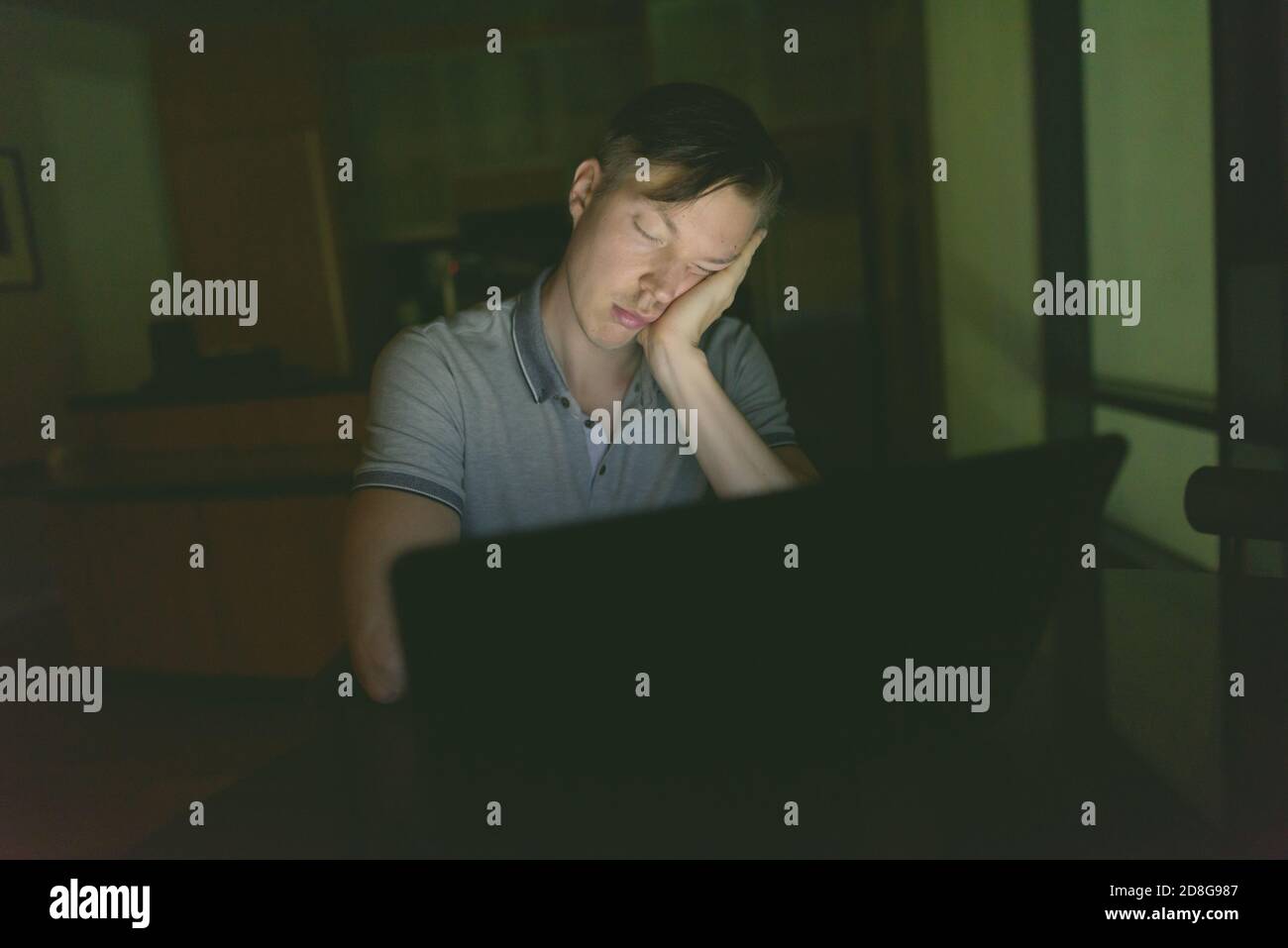 Junger stattlicher Mann mit Laptop im dunklen Wohnzimmer Stockfoto