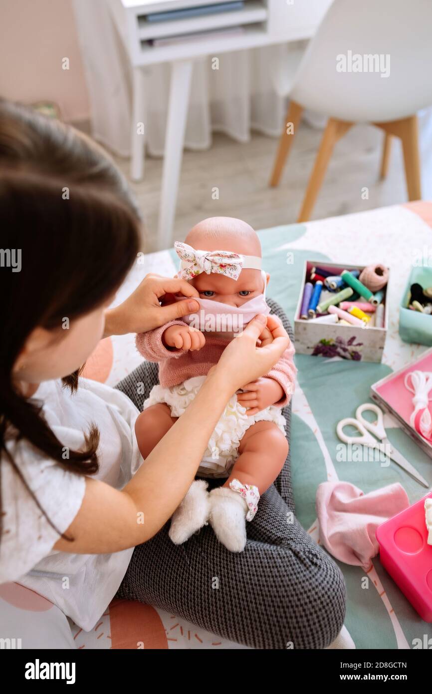 Mädchen versucht auf ihre Puppe eine Maske, die sie ist Nähen Stockfoto