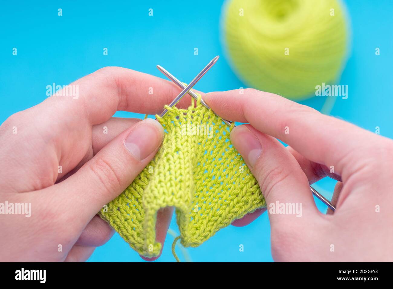 Nahaufnahme weibliche Hände stricken auf einer Stricknadel klassisches Muster aus grünen Fäden auf einem blauen Hintergrund, kopieren Raum Stockfoto