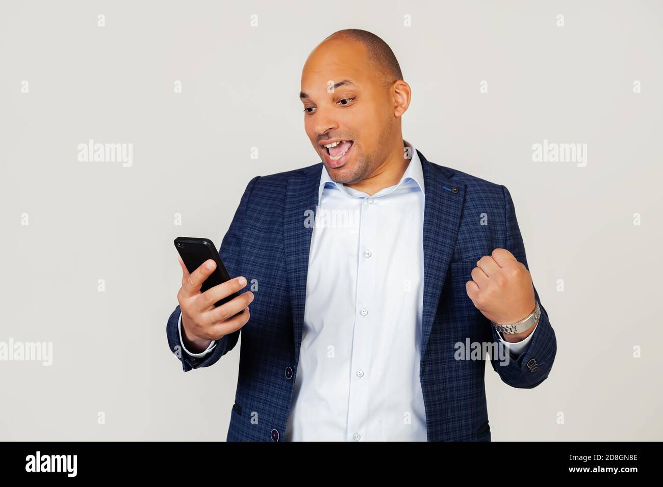 Portrait von glücklichen jungen afroamerikanischen Geschäftsmann Kerl mit Smartphone, schreien mit Stolz und feiern Sieg und Erfolg, sehr aufgeregt, Freude Emotionen. Stehen auf einem grauen Hintergrund. Stockfoto