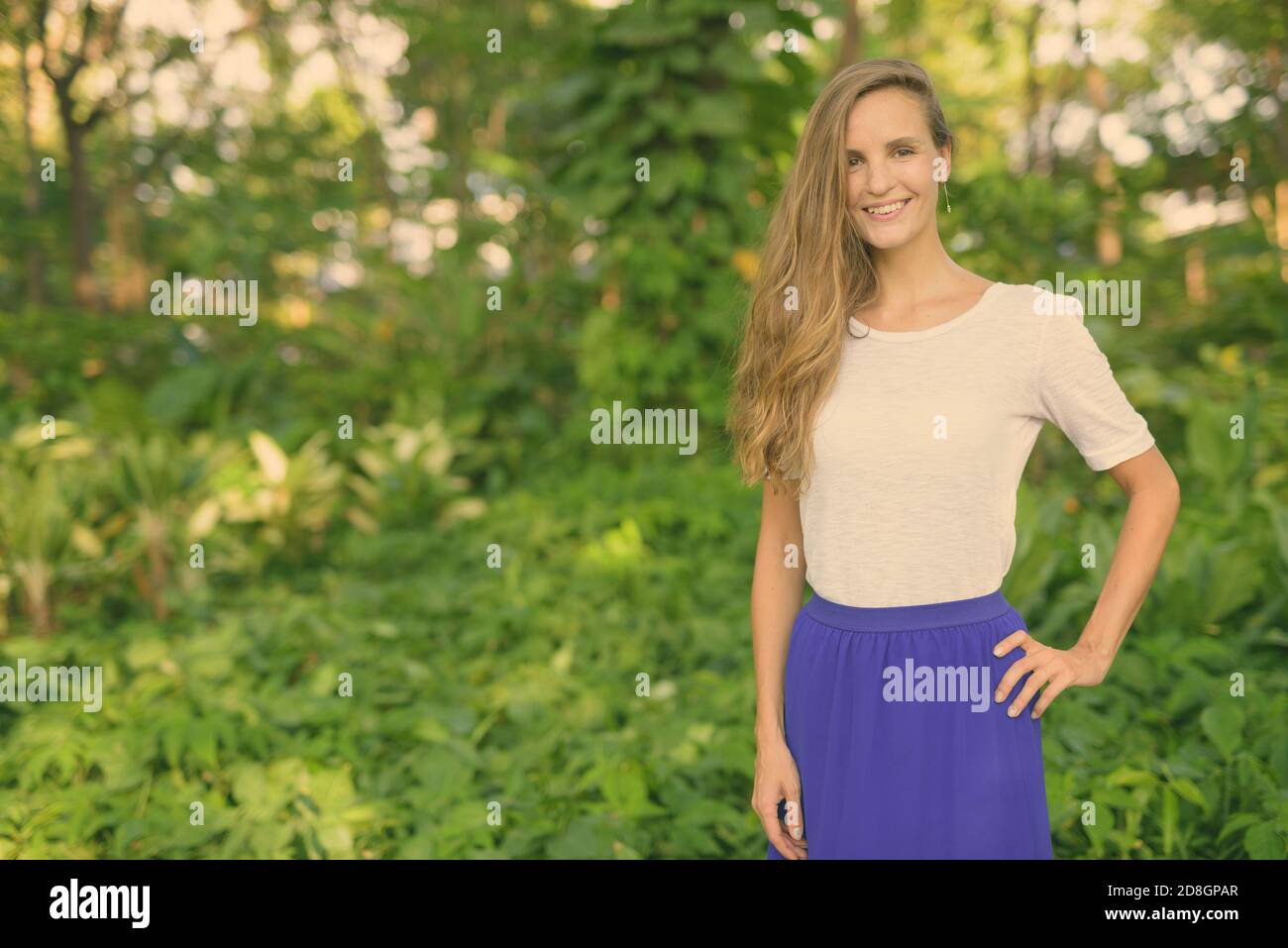 Gerne schöne Frau lächelnd und gegen die malerische Aussicht auf gesunden grünen Garten im Park posing Stockfoto