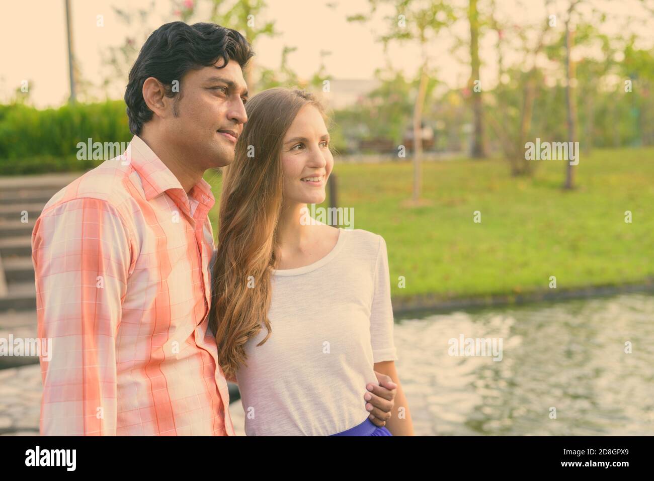Glücklich, multi-ethnische paar Lächeln beim Denken auf Stein Pfad in der Mitte des Sees mit Blick auf die ruhigen, grünen Park Stockfoto