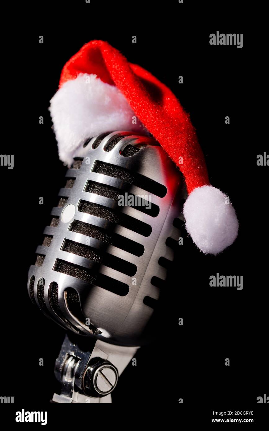 Vintage / Retro Mikrofon trägt einen weihnachtlichen / festlichen Hut, vor einem schwarzen Hintergrund gesetzt. Stockfoto