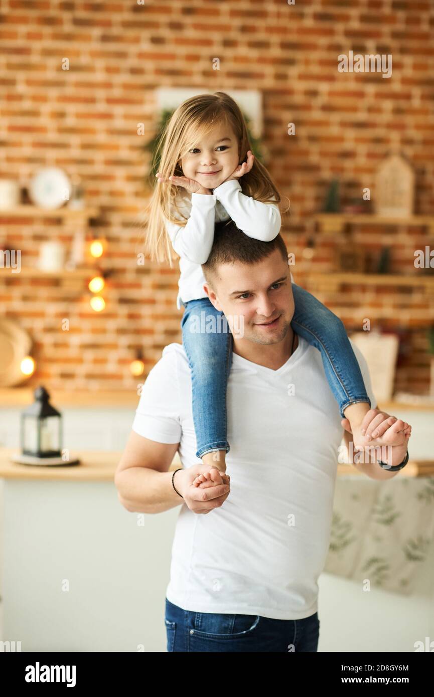 Eine kleine Tochter mit ihrem Vater haben einen Spaß und Spielen in der Küche auf einem Backstein Hintergrund mit einem Verschwommenes Licht Stockfoto