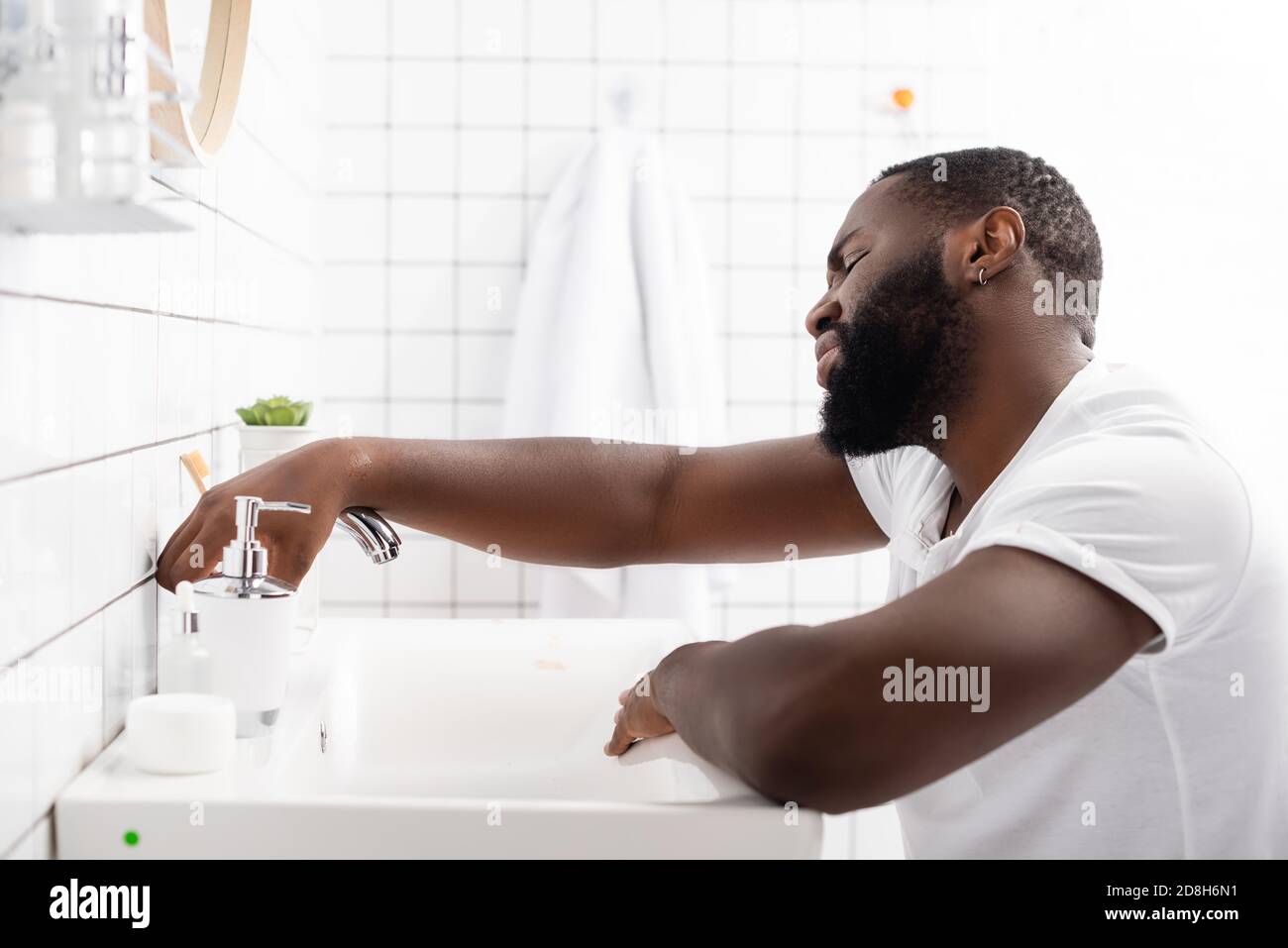 Müder afro-amerikanischer Mann, der sich auf dem Waschbecken lehnte und den  Wasserhahn aufversuchte Stockfotografie - Alamy