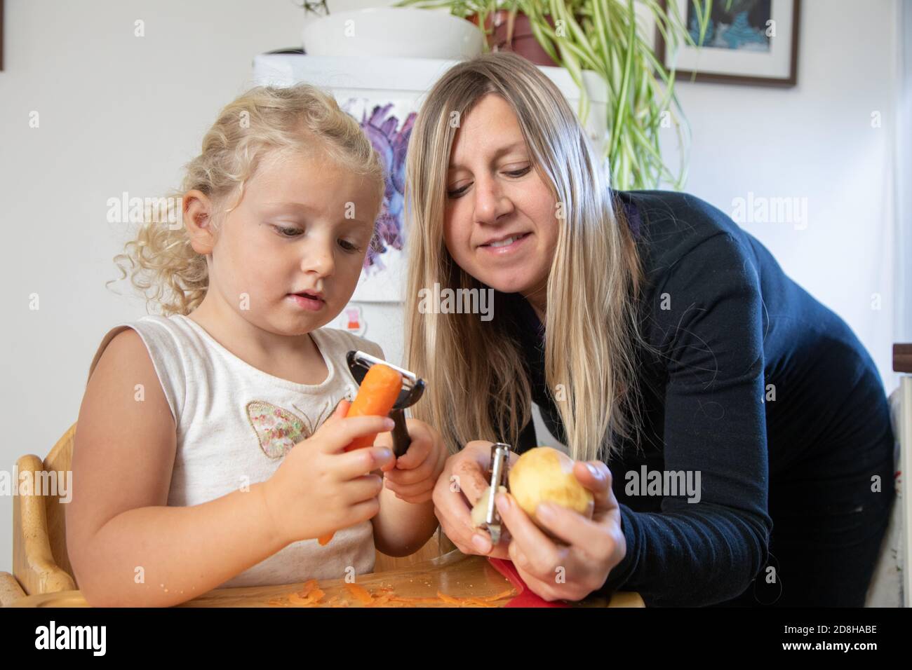 Eine Mutter und eine dreijährige Tochter schälen Gemüse zusammen Stockfoto