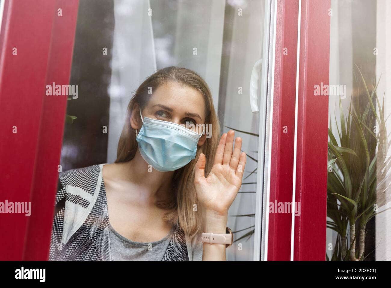 Home Isolation und Quarantäne - Frau mit medizinischer Gesichtsmaske Blick durch das Fenster Stockfoto