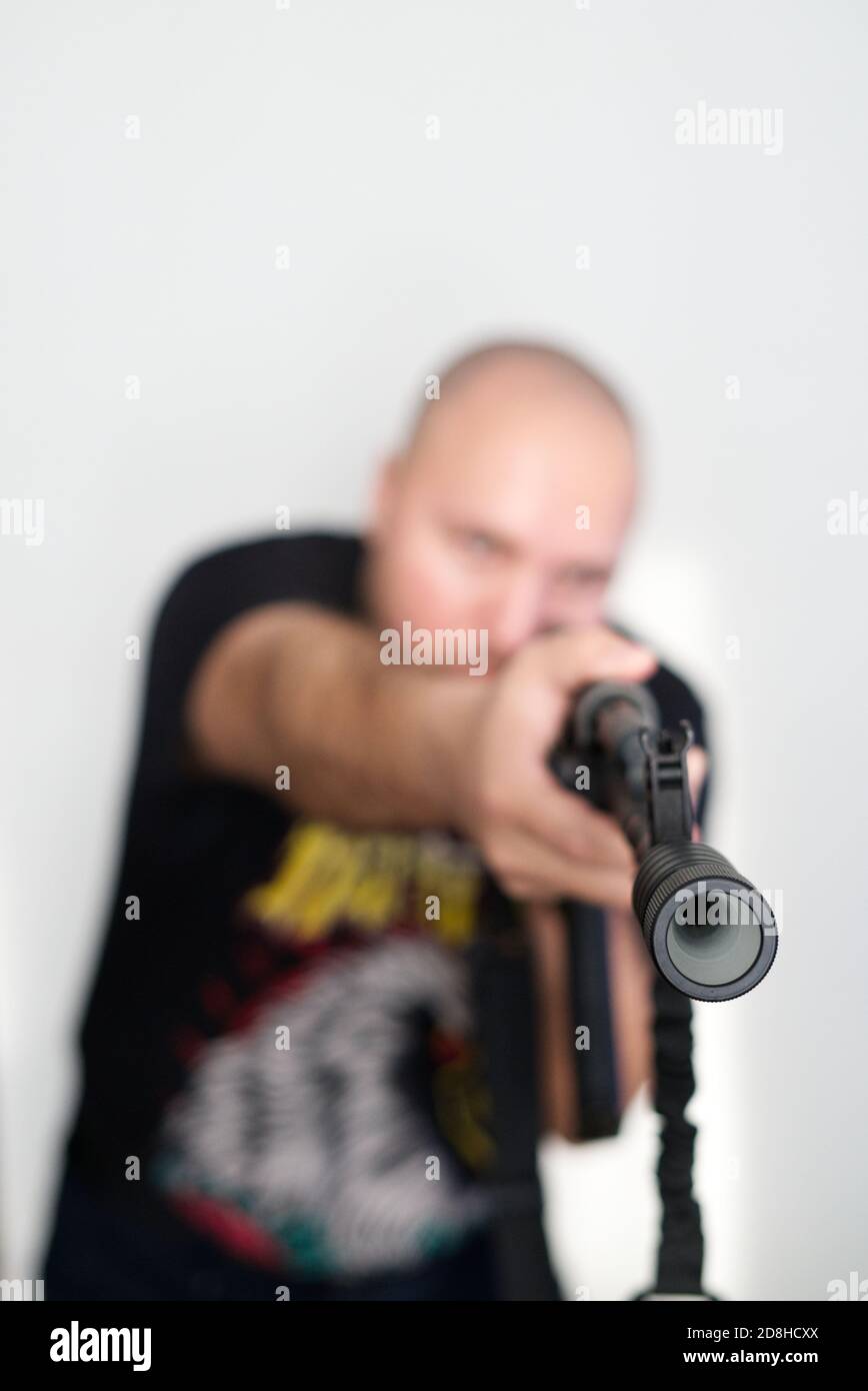 Schwerer verschwommener Mann auf hellem Hintergrund mit Gewehr in den Händen Stockfoto