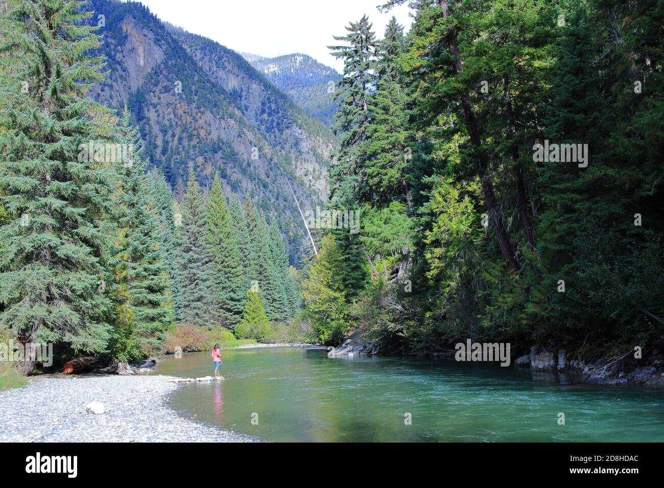 Frau, die am Flussufer in British Columbia, Kanada, steht. Blick auf die Berge. Vollformat, Kopierbereich, Farbfoto. Stockfoto