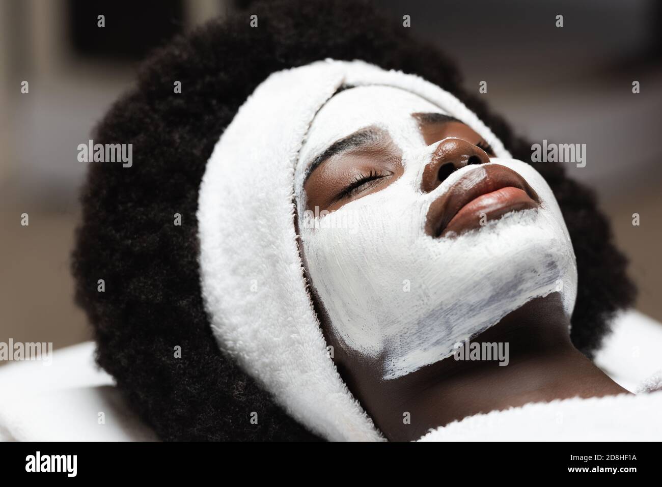 Nahaufnahme der lockigen afroamerikanischen Frau mit Weiß Stirnband und Gesichtsmaske liegen im Spa Salon Stockfoto