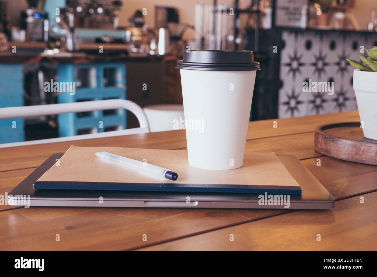 Laptop, Notebook, Stift Heißgetränk Tee oder Kaffee auf dem Tisch im Café. Fernunterricht oder Arbeitskonzept Stockfoto